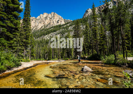 Woman wading through river by Sawtooth Mountains in Stanley, Idaho, USA Stock Photo