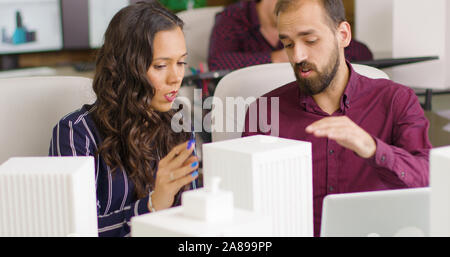 Businessman and creative designer working on 3D printed models of buildings in modern office space Stock Photo