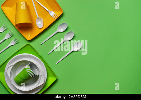 Colorful plastic disposable cutlery, such as plates and bowls, four spoons and forks, folded cups on green background with copy space. The concept of Stock Photo