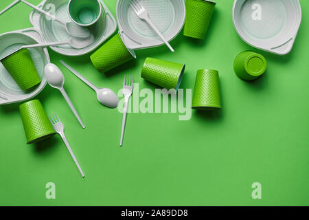 A lot of colorful plastic disposable cutlery, such as bowls, spoons, forks and cups on green background with copy space. The concept of picnic utensil Stock Photo