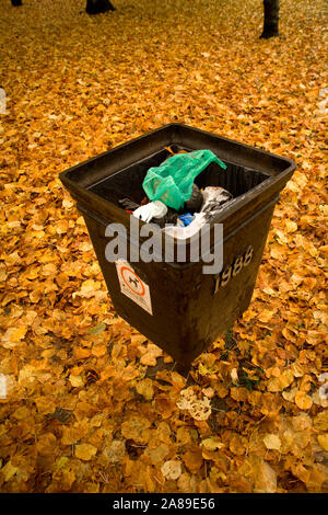 public bin in the UK full of rubbish. The background is golden leaves Stock Photo