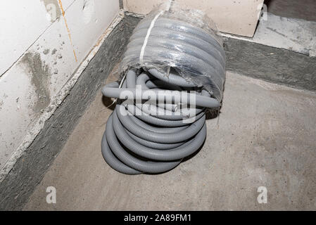 PVC corrugated pipe for electric wires, partly unpacked, lying on the floor in the house. Stock Photo