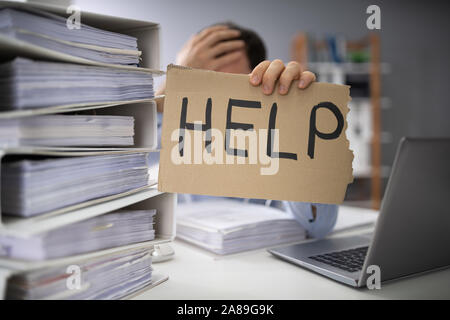 Close-up Of A Businessman Hand Holding Help Sign In Between The Stack Of Folders Stock Photo