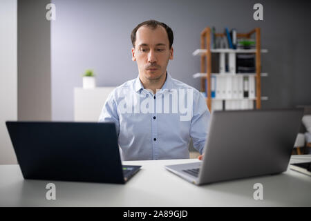 Businessperson Doing Multitasking Work On Two Laptops At Workplace Stock Photo