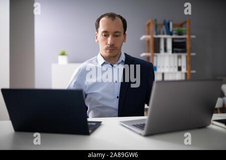 Businessperson Doing Multitasking Work On Two Laptops At Workplace Stock Photo
