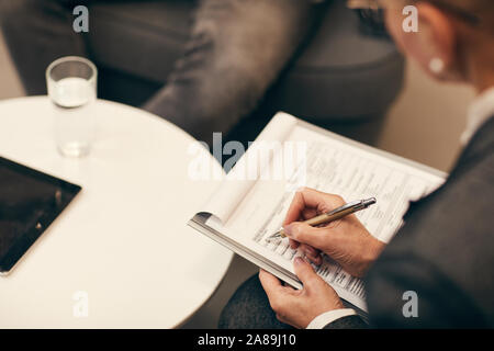 Close-up of mature businesswoman sitting and filling the document during business interview at office Stock Photo