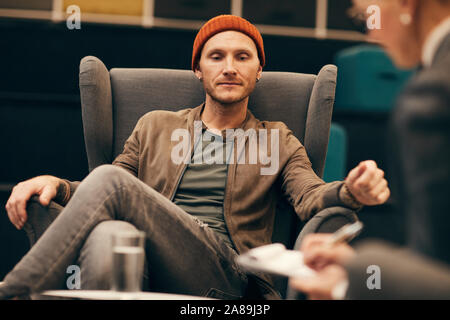 Young confident man in casual clothing sitting on sofa and looking at woman how she making notes in document at office Stock Photo