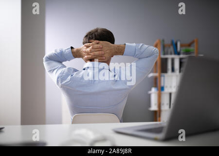 Relaxed Businessman With Hands Behind Head Sitting In Office Stock Photo