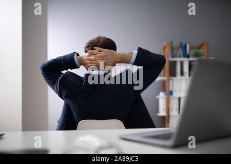 Relaxed Businessman With Hands Behind Head Sitting In Office Stock Photo