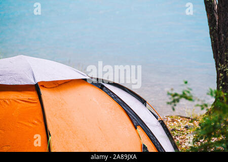 Orange tourist tent on shore of mountain lake. Hiking in forest, tourist equipment for travel Stock Photo