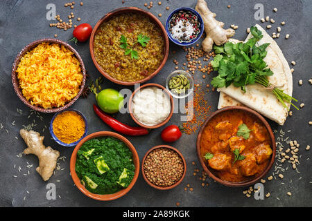 Assorted various Indian food on a dark rustic background. Traditional Indian dishes - Chicken tikka masala, palak paneer, saffron rice, lentil soup, p