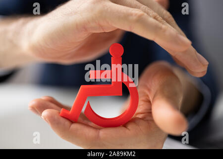 Close-up Of A Person's Hand Protecting Blue Cubic Block With Disabled Icon Stock Photo
