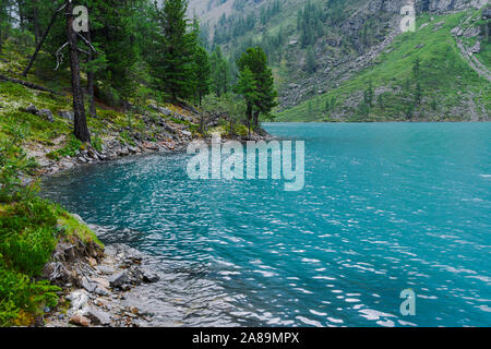 Rocky shore of blue lake. The surf of turquoise sea, waves come to shore Stock Photo