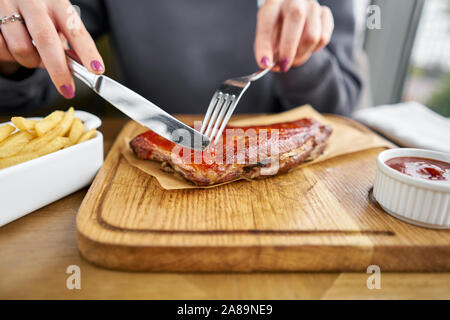 Lunch in a restaurant, a woman cuts Delicious Pork ribs. Full rack of ribs BBQ on wooden plate with french fries and salad Stock Photo