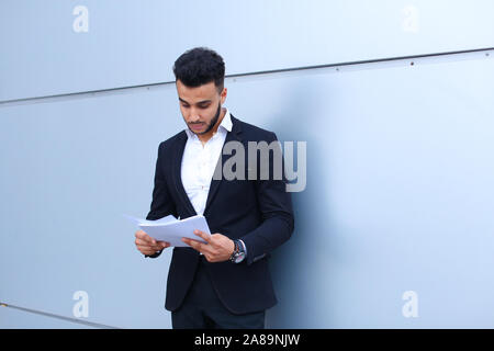 Arabian Successful businessman holds documents, smiling little smile and thinks near wall of business center. Stock Photo