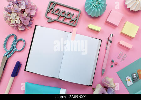 Top view flat lay with various colorful office supplies like pencils, scissors, notepads, pins and open empty notebook as placeholder for text on pink Stock Photo