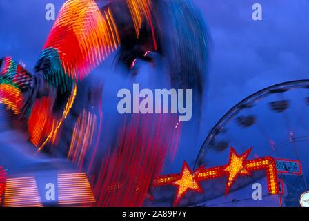 Whirling, neon lit carnival ride at dusk Stock Photo