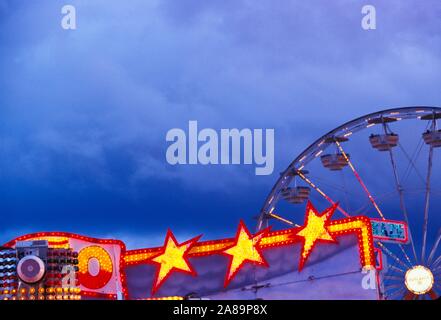 Whirling, neon lit carnival ride at dusk Stock Photo