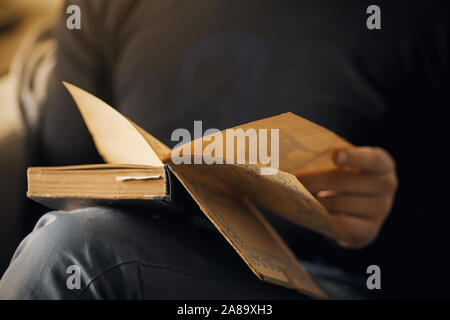 A man in dark clothing and jeans sits and holds in the hands of open old book, that intends to to read. Stock Photo