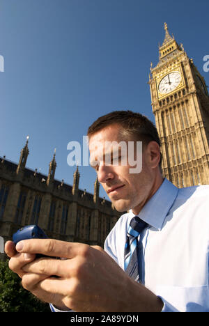Young businessman in shirt and tie stands texting in front of the London skyline with Big Ben and the Houses of Parliament on a bright sunny day Stock Photo
