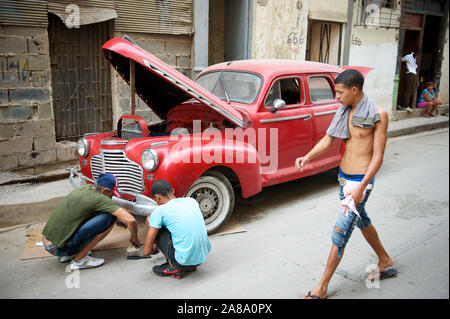 HAVANA - MAY 18, 2011: Cuban men squat in the street next to a vintage red car with its hood propped open for repair. Stock Photo