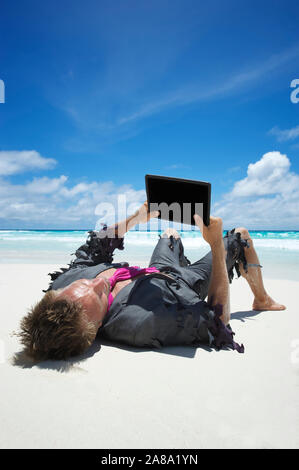 Castaway businessman relaxing with wifi on a tropical beach using his tablet computer Stock Photo