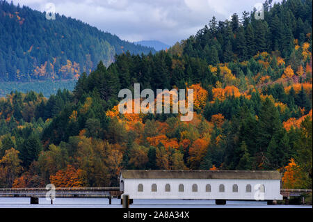 Autumn colors in the Cascade Mountain Range, where a covered bridge sits along the shore of a lake Stock Photo