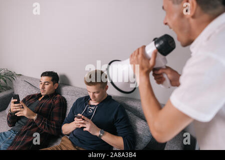 Young man screams through a megaphone at friends which using a mobile phone. Stock Photo