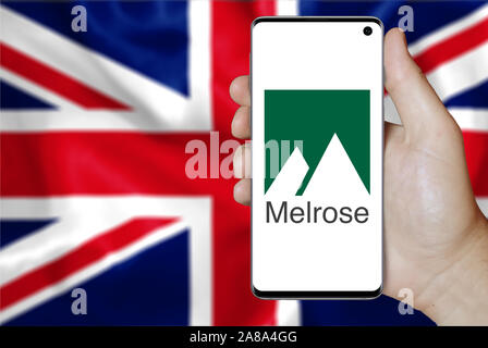 Logo of public company Melrose Industries displayed on a smartphone. Flag of UK background. Credit: PIXDUCE Stock Photo