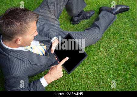 Young businessman reclining on green grass lawn using his tablet computer Stock Photo