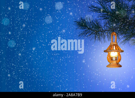 Christmas background with wooden lantern on pine tree branch at snowfall. Christmas and New Year greeting card or beautiful winter blue night backdrop Stock Photo