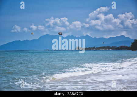 Parasailing on the waves of the azure Andaman sea under the blue sky near the shores of the sandy beautiful exotic and stunning Cenang beach in Langka Stock Photo