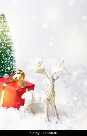 Snowy Christmas greeting card with red gift box tied golden bow and figurine of reindeer with place for text. New Year background. Stock Photo
