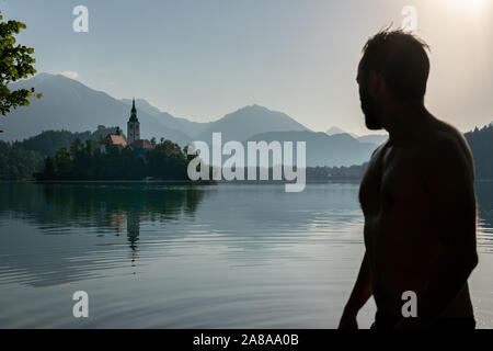 Silhouette of an European man observing the beauty of the Bled Island, while bathing in lake Bled Stock Photo