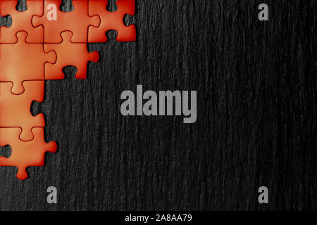 Red puzzle in the corner of the image on a black natural stone background of slate. A frame with an empty space for your description. Stock Photo