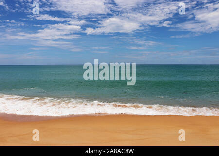 Tropical sandy beach, scenic view to empty sea coast with yellow sand and emerald wave with white foam. Picturesque seascape with blue sky Stock Photo