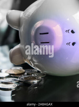 Sad and very tired piggy bank is lying on the side, next to few coins. Stock Photo