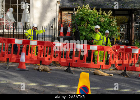 Three Builders in high visibility clothing behind a barrier in the road standing around talking Stock Photo