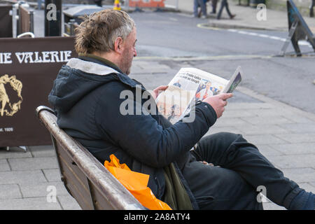 A man sitting on a bench reading a newspaper Stock Photo