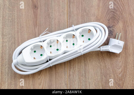 New four outlets power extension cord on a wooden surface. White electric power strip for home or office. Household appliances. Top view. Stock Photo