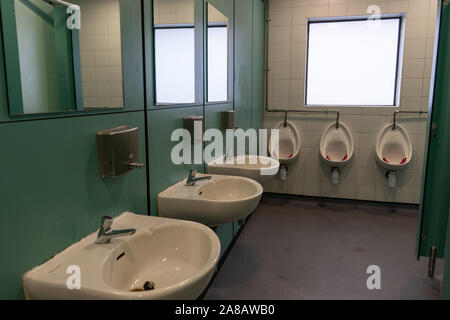 The interior of an empty public toilet or bathroom with sinks and urinals