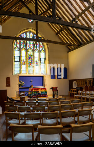 The altar of an anglican church with a stained glass window behind surrounded by chairs Stock Photo
