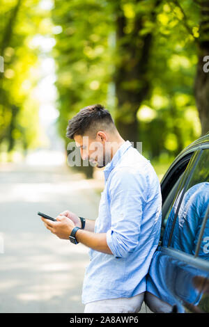 Handsome man standing and using the phone with his car. Stock Photo