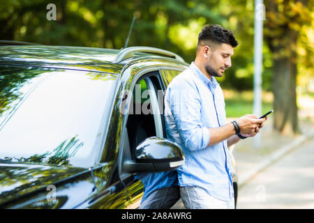 Handsome man standing and using the phone with his car. Stock Photo