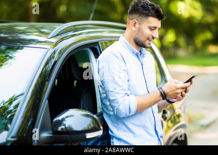 Handsome man standing and using the phone with his car. Stock Photo