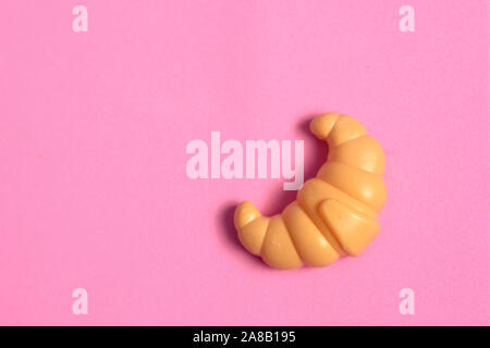 Toys for kids in food theme. One Croissant on pink background. Food and toy concept. Object made from plastic. Stock Photo