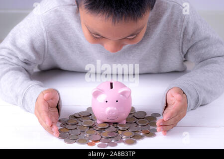 Asian boy looking to piggy bank and various coins. Saving money concept. Stock Photo