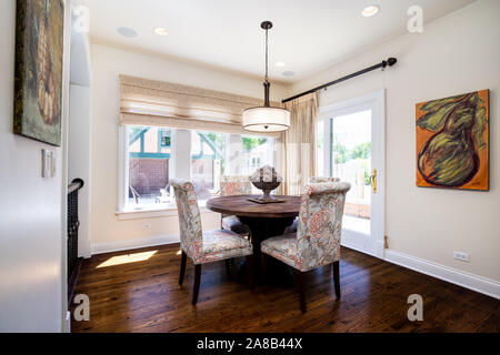 A dining room with a circular table, patterned chairs, hardwood floors, and art hanging on the walls. Stock Photo