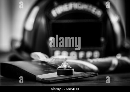 A teardrop, or pear, shaped diamond engagement ring on top of a wedding band and fireman's ax with a firefighter helmet blurred in the background. Stock Photo