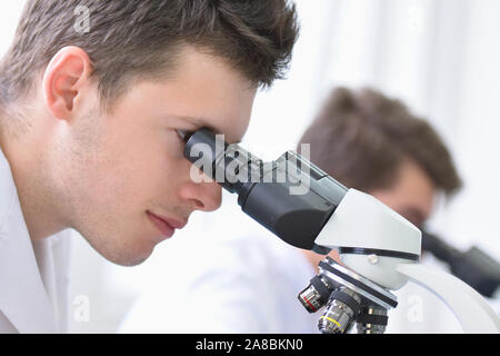 Two Young male scientists looking through a microscope in a laboratory doing research, microbiological analysis, medicine. Stock Photo